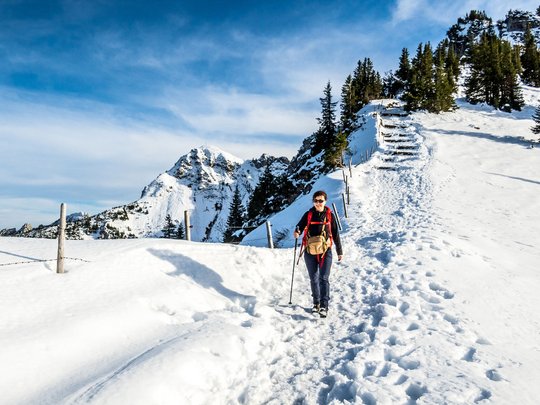 Mit einem Lächeln aufstehen im Hotel am Spitzingsee Frau wandert auf schneebedecktem Bergweg mit Bergen und Bäumen im Hintergrund