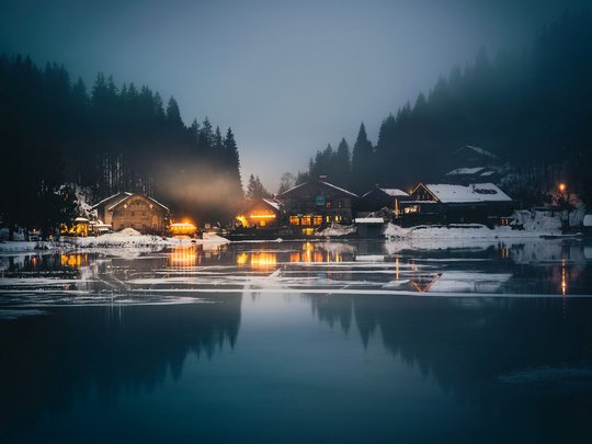 Mit einem Lächeln aufstehen im Hotel am Spitzingsee Dorf am zugefrorenen See bei Nacht mit beleuchteten Häusern und verschneitem Wald