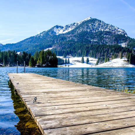 A look at Alte Wurzhütte Wooden pier extending into a mountain lake with snow-covered peaks in the background