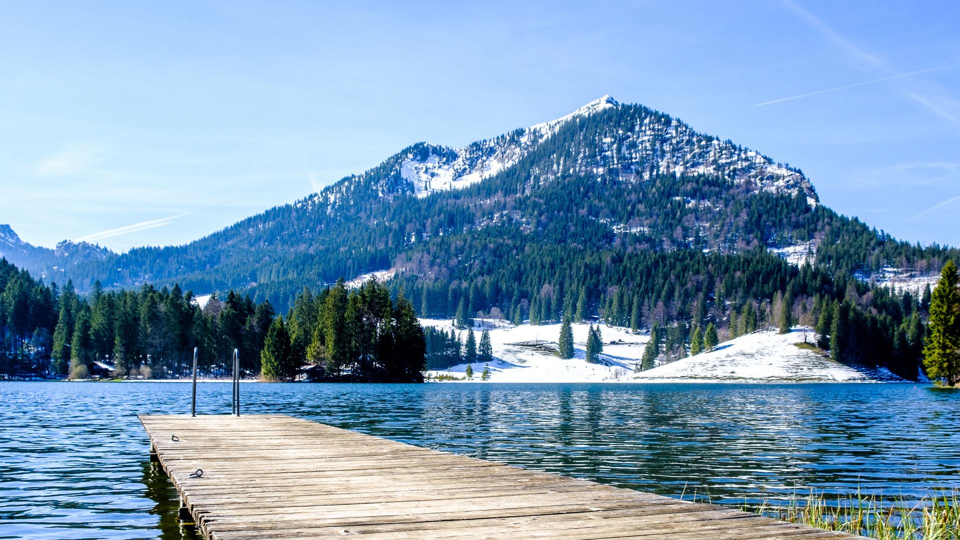 Holzsteg auf einem Bergsee mit schneebedeckten Gipfeln im Hintergrund