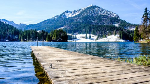 Apartment mit Terrasse Holzsteg auf einem Bergsee mit schneebedeckten Gipfeln im Hintergrund