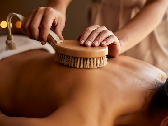 Massagen und Sauna am Spitzingsee Person erhält Rückenmassage mit Bürste in entspannter Atmosphäre