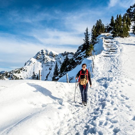 A look at Alte Wurzhütte Woman hiking on snowy mountain trail with mountains and trees in the background