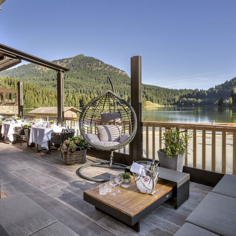 A look at Alte Wurzhütte Cozy terrace with lake view, hanging chair and dining tables against mountain backdrop