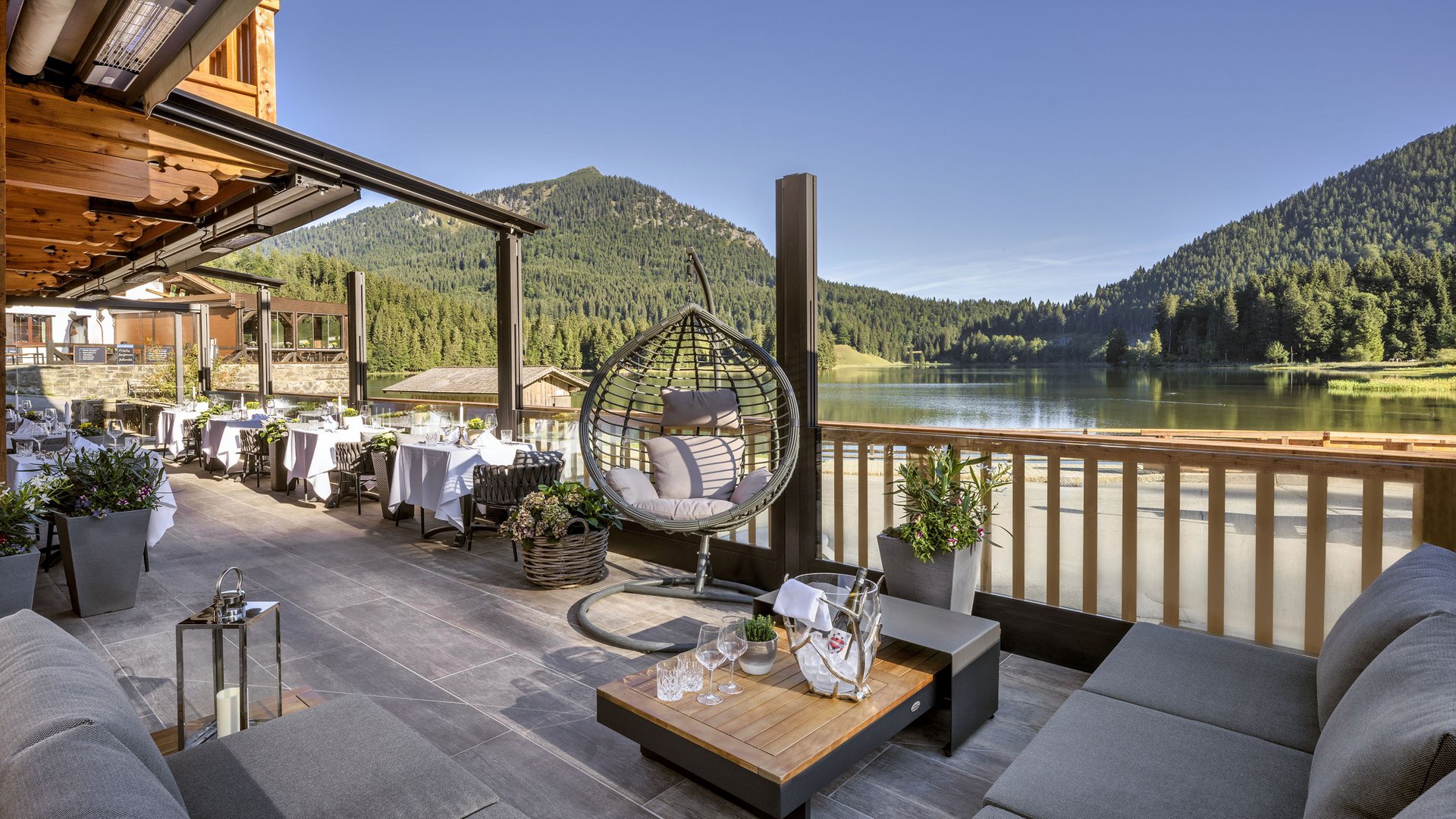 Gemütliche Terrasse mit Seeblick, Hängesessel und Tischen vor Bergkulisse
