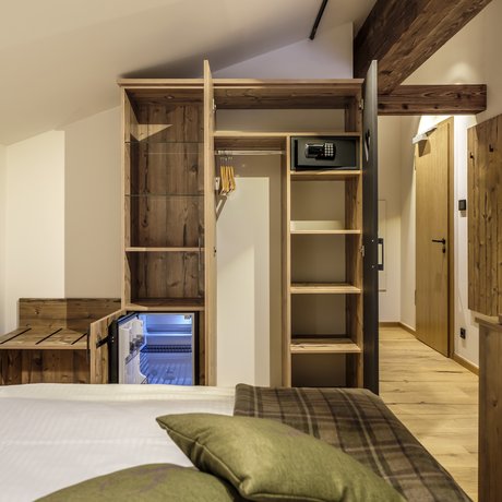 A look at Alte Wurzhütte Hotel room with open wardrobe, safe, minibar, wooden furniture, and bed in foreground
