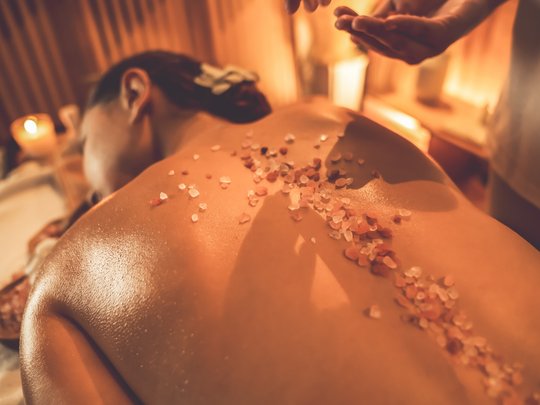 Massagen und Sauna am Spitzingsee Frau beim Salzmassage-Spa mit warmem Kerzenlicht im Hintergrund