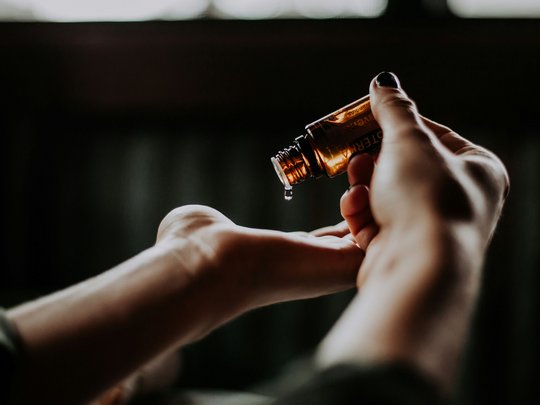 Massagen und Sauna am Spitzingsee Hand tropft Öl aus einer kleinen braunen Flasche auf die andere Hand