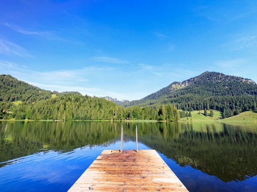 Mit einem Lächeln aufstehen im Hotel am Spitzingsee Steg an einem ruhigen See mit Bergblick und klarem Himmel