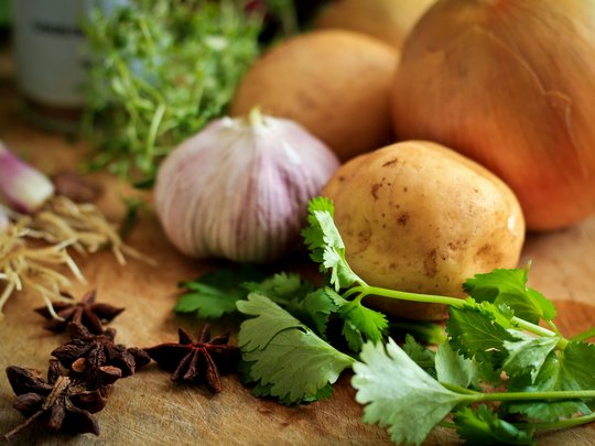 The perfect menu for your event Potatoes, onions, garlic, star anise and fresh herbs on cutting board