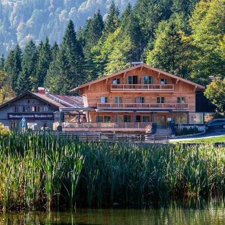 A look at Alte Wurzhütte Wooden house by lake with mountains and forest in the background