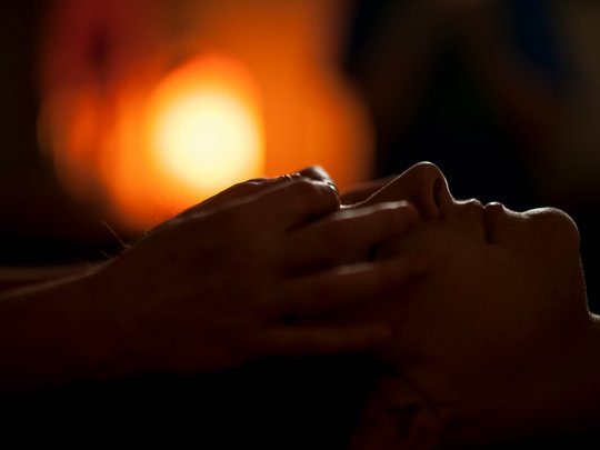 Massagen und Sauna am Spitzingsee Gesicht einer Person im Profil mit warmer Beleuchtung und einer Hand auf der Stirn
