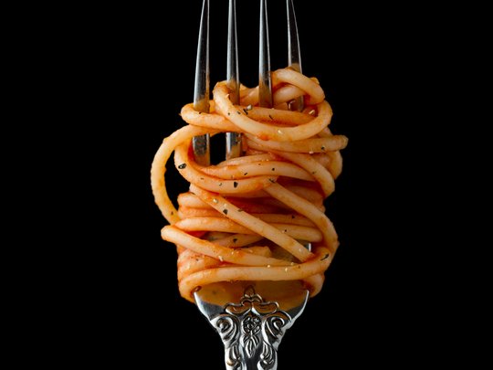 The perfect menu for your event Spaghetti with tomato sauce wrapped around a silver fork on black background
