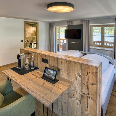 A look at Alte Wurzhütte Bright hotel room with wooden furniture, desk, armchair, and lake view