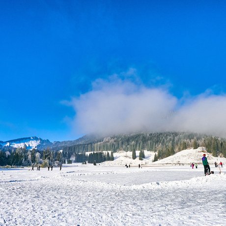 A look at Alte Wurzhütte People skating and playing hockey on a frozen lake in a snowy mountain landscape