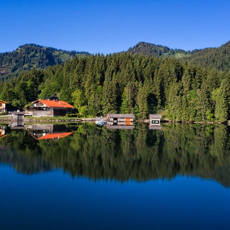 A look at Alte Wurzhütte Reflection of houses and trees in a calm mountain lake under clear blue sky