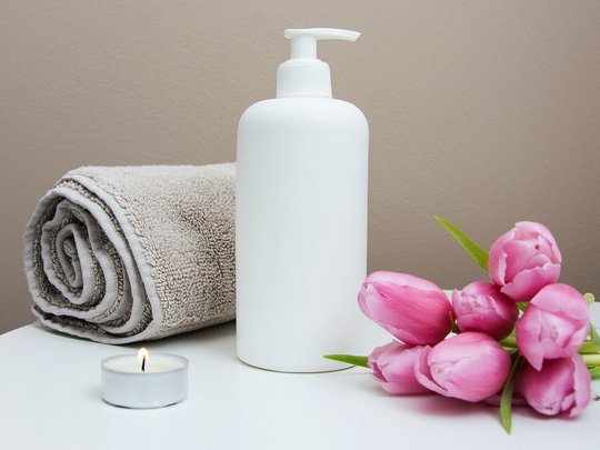 Massagen und Sauna am Spitzingsee Weiße Lotionflasche mit Handtuch, brennender Kerze und pinken Tulpen auf Tisch