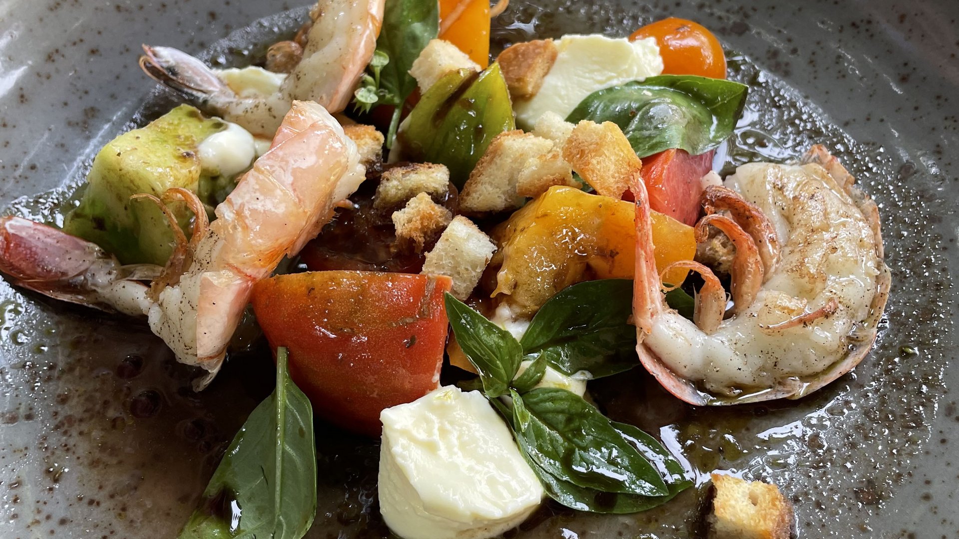 Garnelensalat mit Tomaten, Mozzarella, Basilikum und Croutons auf einem grauen Teller