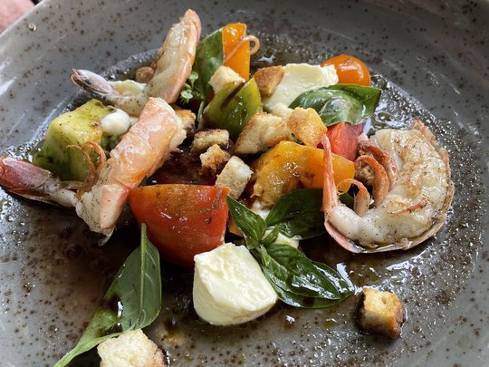 The perfect menu for your event Shrimp salad with tomatoes, mozzarella, basil, and croutons on a gray plate