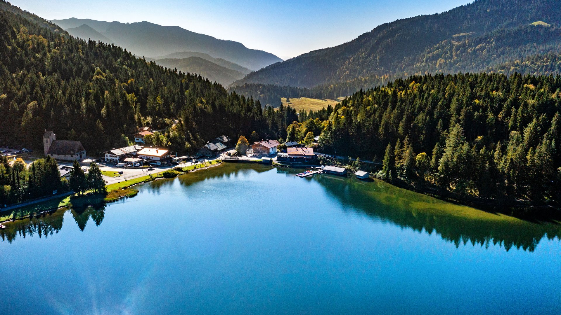 View of a calm mountain lake surrounded by forest and mountains on a clear day