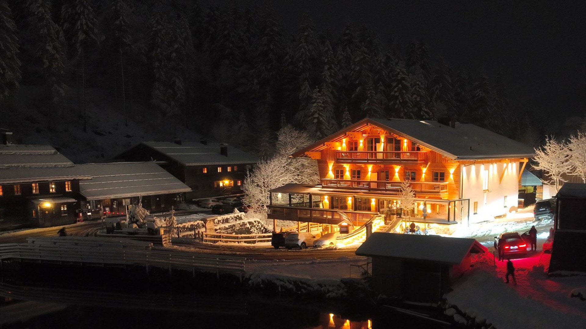 Illuminated house and snowy landscape at night with cars and trees